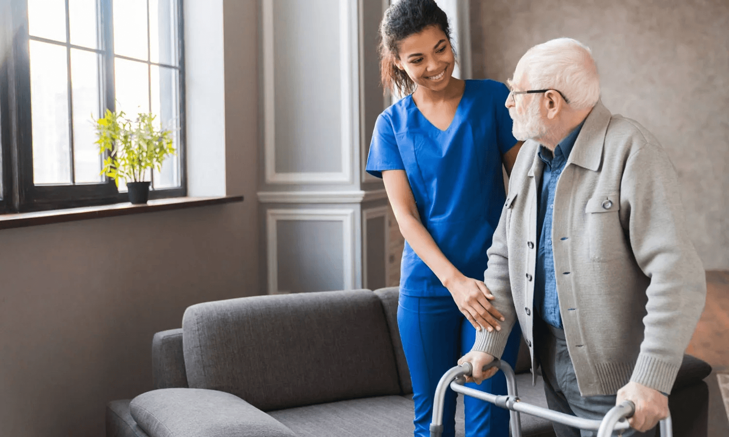 A carer supporting an older man with a walking frame at home